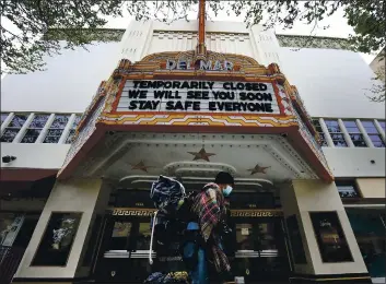  ?? SHMUEL THALER — SANTA CRUZ SENTINEL FILE ?? A man wearing a mask carries his belongings in March 2020 past the Del Mar Theater on Pacific Avenue in Santa Cruz, where the marquee presents a message of community caring.