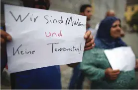  ??  ?? ANSBACH: Refugees from Syria stand near the site of the attack and hold up a sign reading ‘we are Muslims and not terrorists’. — AP