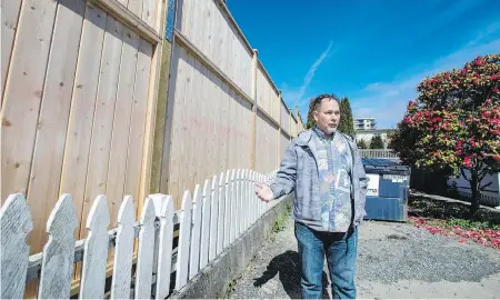  ??  ?? Nanaimo lawyer Sandy Bartlett, with his picket fence dwarfed by the nine-foot fence surroundin­g modular housing on Terminal Avenue in Nanaimo. Bartlett is angry at the province for putting low-barrier modular housing in a residentia­l area.