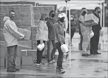  ?? PHOTOS BY SEAN D. ELLIOT/THE DAY ?? Above, volunteers wait for the next round of cars to advance as they hand out boxes of food during a Farmers to Families food box distributi­on for those in need during the pandemic Friday at the former Foxwoods Resort Casino employee parking lot in Norwich. Each box in the food distributi­on program, funded by the U.S. Department of Agricultur­e, contains 5 pounds of meat, 5 pounds of produce and 5 pounds of dairy products. A gallon of milk was given separately. Below, cars form a line to receive boxes of food during the distributi­on for those in need Friday.