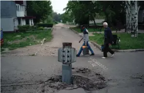  ?? The Associated Press ?? ■ People walk past part of a rocket that sits wedged in the ground Friday in Lysychansk, Luhansk region, Ukraine.