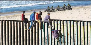  ?? Nelvin C. Cepeda San Diego Union-Tribune ?? CENTRAL AMERICANS climb the fence between Mexico and California as U.S. Border Patrol officers watch. About 400 migrants arrived by bus in Tijuana this week. Most are expected to request asylum.