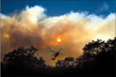  ?? AP/NOAH BERGER ?? Smoke billows from the Camp Fire as a firefighti­ng helicopter hovers Sunday near Pulga, Calif.