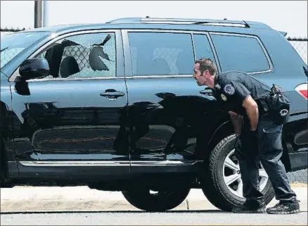  ?? ALEX WONG / AFP ?? Un policía se protege junto a un coche con la ventanilla rota por un disparo ayer en Alexandria
