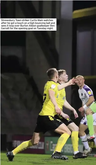  ??  ?? Shrewsbury Town striker Curtis Main watches after he got a touch on a high bouncing ball and sees it loop over Burton Albion goalkeeper Ben Garratt for the opening goal on Tuesday night.