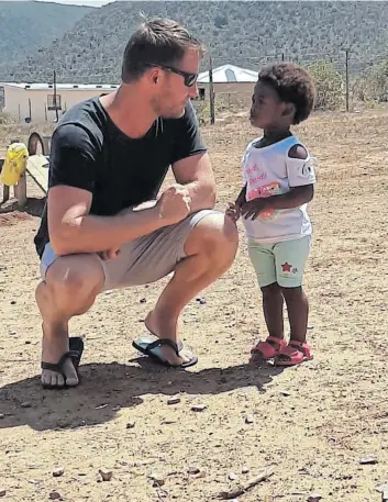  ?? Pictures: ADRIENNE CARLISLE ?? BONDING: Cameron shares a moment with one of his tiny admirers at Sakhisizwe Early Childhood Developmen­t Centre in Pikoli village near Peddie.