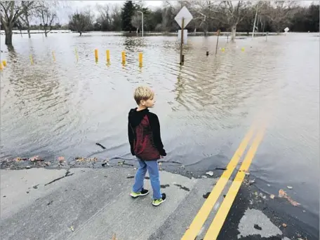  ?? Gary Coronado Los Angeles Times ?? JACK RYAN and his family came out to behold the water cresting the south bank of the American River, f looding the American River Parkway in Sacramento’s Discovery Park. “I have not seen this for a long time,” said Ron Ryan, Jack’s father. “It is kind...