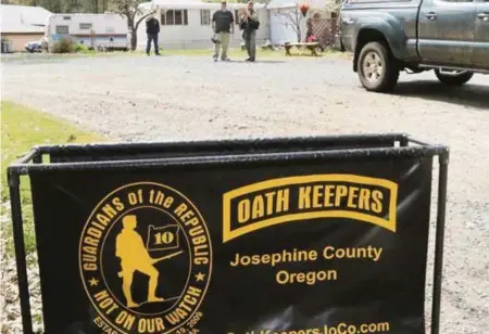 ?? Timothy Bullard ?? On April 14, 2015, an Oath Keepers sign marks the entrance to a property near Merlin, Ore, while armed Oath Keepers security guards hover in the background.