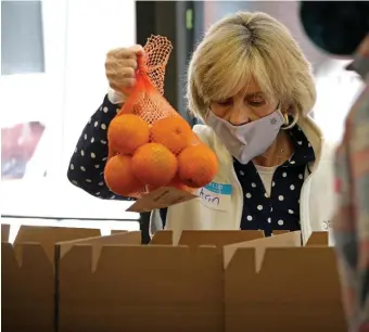  ?? STuART CAHILL pHOTOs / HeRALd sTAFF ?? SQUARE MEALS: Ann Conner packs oranges as part of Food for Free’s efforts in Cambridge. At left from left, Toyesi Saint-Cyr, Bob O’Reilly and Julio Cesar Franico load boxes with food.