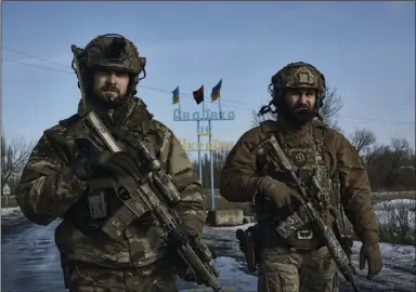  ?? (AP/Libkos) ?? Ukrainian soldiers walk against the background of a sign reading “Avdiivka is Ukraine” close to the frontline Sunday in Avdiivka, in the Donetsk region, Ukraine. Ukraine and some U.S. officials are blaming Russia for slowing down inspection­s as the war nears the one-year mark.