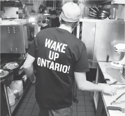  ?? JEAN LEVAC / POSTMEDIA NEWS FILES ?? Nick Thompson in the kitchen at the Black Tomato restaurant in Ottawa wearing a “wake up Ontario” slogan. Owner Peter Besserer closed the restaurant citing higher minimum wage, which he says would have cost him $80,000 a year.