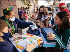  ?? WADE VANDERVORT ?? Teacher Candy Collins-adams, left, hands out toys and shoes Dec. 17 during a drive-thru charity event sponsored by local philanthro­pists Bob and Sandy Ellis at Martinez Elementary School in North Las Vegas.