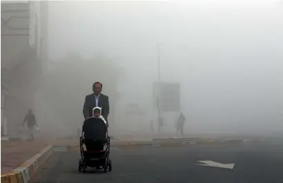  ?? Photo by Ryan Lim ?? A father takes his child out through fog in Abu Dhabi on Monday. The weather will continue to be foggy till Friday. —