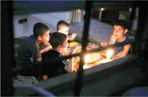  ??  ?? A Palestinia­n family eats dinner by candleligh­t at their makeshift home in the Rafah refugee camp, in the southern Gaza Strip, during a power outage on Sunday. (AFP)
