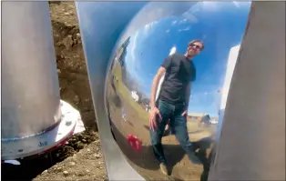  ?? NEWS PHOTO GILLIAN SLADE ?? Andy Davies, artist, is reflected in one of the highly polished sphere’s representi­ng seeds in the Prairie Shoots.