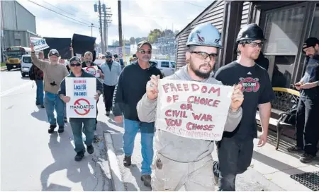  ?? JOSH REYNOLDS/AP ?? Justin Paetow, front, holds a sign while a group protests against a COVID-19 vaccine mandate Friday at Bath Iron Works in Bath, Maine.