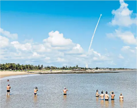  ??  ?? Beachgoers in Kourou, French Guiana, take pictures as an Ariane 5 space rocket with a payload of four Galileo satellites lifts off from ESA’s European Spaceport