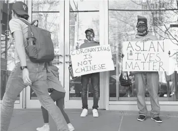  ?? MICHAEL M. SANTIAGO/GETTY ?? Cameron Hunt and his father, Calvin Hunt, hold signs of support as they stand Tuesday near the spot where an Asian American woman was attacked Monday in New York City. The NYPD is calling the attack a hate crime.