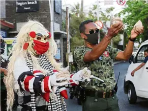  ?? — AP ?? Social cues: A man in a Balinese ‘celuluk’ costume with a facemask offering free wrapped rice during a campaign to promote wearing masks in Bali. Making sure Covid-19 precaution­s take social context into account is important in ensuring adherence.