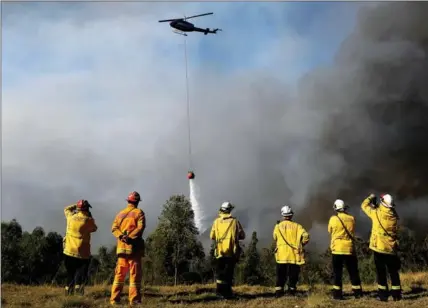  ?? AAP IMAGE / DAN HIMBRECHTS / VIA REUTERS ?? Firefighte­rs watch as a helicopter drops water to protect properties last month in Colo Heights, northwest of Sydney, Australia.