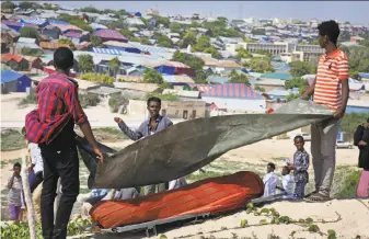  ?? Farah Abdi Warsameh / Associated Press ?? Somali men cover the body of a victim of a suicide-bomb attack before burial after a man disguised as an officer attacked a police academy in the capital, Mogadishu.