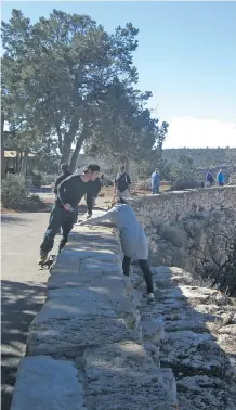  ??  ?? A young tourist heads back over a retaining wall to safety on the South Rim path of the Grand Canyon after being admonished by a National Park giftshop cashier. Over the years, dozens of tourists have fallen to their death.