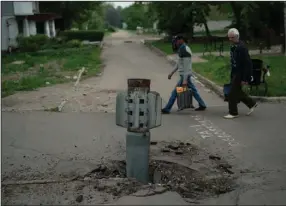  ?? (AP /Leo Correa) ?? People walk past part of a rocket that sits wedged in the ground in Lysychansk, Ukraine, on Friday.