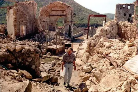  ?? (AFP/Getty) ?? A gir l carries jugs of water down a street destroyed by Croat she ll ing near the o l d bridge in the eastern (Mus l im) part of Mostar, 30 March 1994