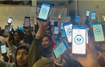  ?? ELLIOT SPAGAT/AP ?? Migrants hold up their phones showing the CBPOne app at a shelter Jan. 22 in Tijuana, Mexico. The mobile app intended for migrants to seek asylum in the United States has been overwhelme­d since it was introduced this month.