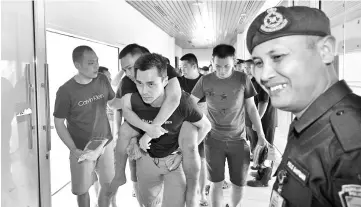  ??  ?? Mark Roger being carried by a friend after suffering a leg injury when they arrived in Kuching Internatio­nal Airport. - Bernama photo