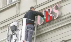  ?? — Reuters ?? A man cleans the logo of Swiss bank UBS on a branch in Bern