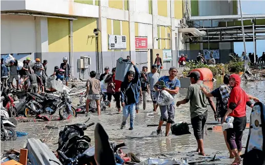  ?? AP ?? People carry looted items from a shopping mall which was damaged following earthquake­s and tsunami in Palu, Central Sulawesi.