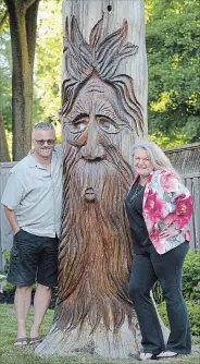  ??  ?? Ron Hiegelsber­ger and Kari Bennett with their uniquely carved 12-foot pine stump. An ice storm a few years ago destroyed the rest of the large tree but a friend, S.T. Thomson, came in and personaliz­ed what was left. The whimsical carving is a focal point in their front garden.