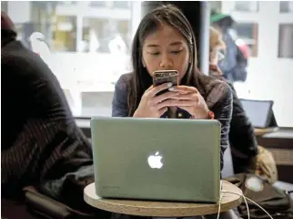  ?? /Reuters ?? Weaker demand: A woman uses her Apple iPhone and laptop in a cafe in New York City. Apple’s shares have fallen 6% this year as it struggles with weak iPhone demand and tough competitio­n in China.