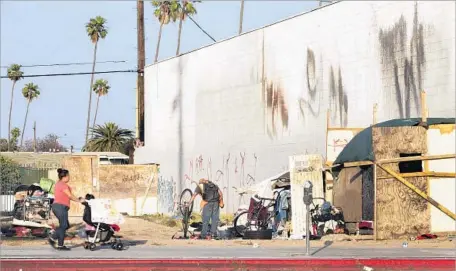  ?? Gina Ferazzi Los Angeles Times ?? A WOMAN pushes a carriage in front of a homeless encampment in the vacant lot near Vermont and Manchester. When officials announced their plans for an entertainm­ent district on the property, many residents cheered. The project was set to open by the end of 2016.