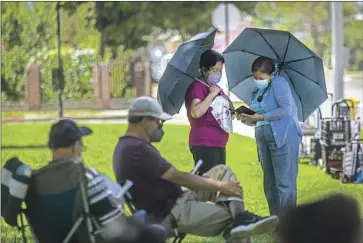  ?? Photograph­s by Francine Orr Los Angeles Times ?? IN TONY ARCEO Memorial Park, named for an El Monte police officer killed in the line of duty in 1974, Elsa De Los Rios, 70, standing at left, and Pily Cuevas, 78, are among those waiting for a church food delivery.