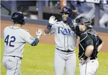  ?? WILFREDO LEE/AP ?? The Rays’ Yandy Diaz, center, congratula­tes Yoshitomo Tsutsugo, left, after Tsutsugo hit a two-run home run scoring Diaz as Marlins catcher Chad Wallach, right, looks on during Sunday’s game in Miami.