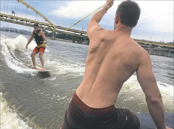  ?? Bob Batz Jr./Post-Gazette photos ?? Duff Cooper helps coach first-time wakesurfer Jay Shadron on the Monongahel­a River during a Pass the Handle event.