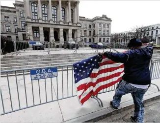  ??  ?? Robert Boens of Atlanta unfurls a U.S. flag Sunday at Georgia Capitol barricades. High security is expected to last through Wednesday’s inaugurati­on of President-elect Joe Biden.