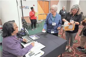  ?? MIKE DE SISTI / MILWAUKEE JOURNAL SENTINEL ?? Pat McFarland, center, with Interfaith Conference of Greater Milwaukee, gets cash from the bank from Sheilah Lewis, a direct service provider for the Social Developmen­t Commission. Lewis plays a banker as Jennifer Russell, right, of Marquette University waits in line.