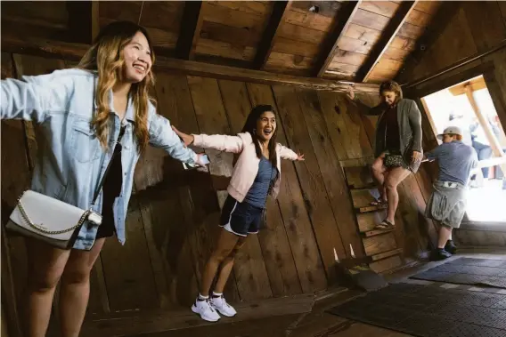  ?? LAURA MORTON ?? Pamela Bernardo, left, and Myline Olivas pose for photos while visiting The Mystery Spot, a tourist attraction that describes itself as a “gravitatio­nal anomaly” in Santa Cruz.