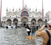  ??  ?? Tourists at the flooded St Mark’s Square in Venice, Italy, recently.