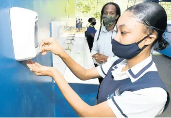  ??  ?? Junior Education Minister Alando Terrelonge looks on as Cedar Grove Academy student Lechelle Walker sanitises her hands yesterday as schools across the island reopened to students sitting external examinatio­ns.