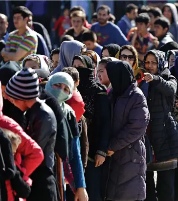  ??  ?? Desperate: Refugees and migrants wait to receive food distribute­d by the Greek army