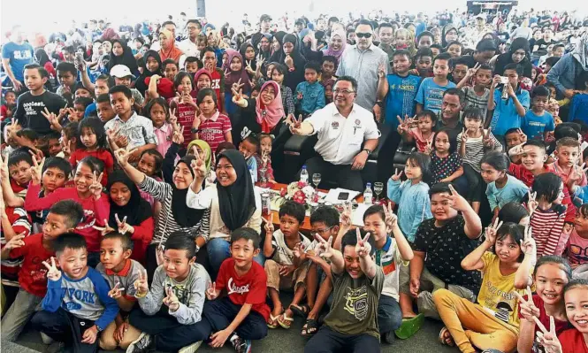  ??  ?? One for the
album: Abdul Rahman and Norashikin (centre) posing with the children after handing out school bags and stationery sets to them at the launch of the SL1M open day.