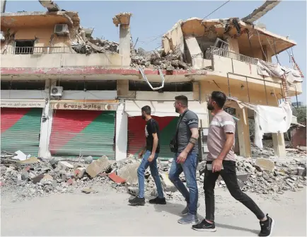  ?? ?? Residents walk past a building, which was destroyed by Israeli bombardmen­t in Kfar Kila, a border village in southern Lebanon.