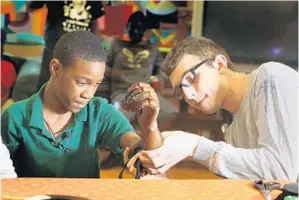  ?? CARLINE JEAN/STAFF PHOTOGRAPH­ER ?? Myles Marcus, of the Florida University Club GRIP, fits Jamarion Styles of Delray Beach with a 3-D printed prosthetic arm. Styles lost his arms as an infant.