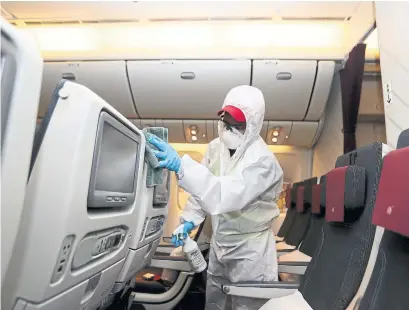  ?? KARIM JAAFAR AFP/GETTY IMAGES FILE PHOTO ?? An employee of Qatar Aviation Services wearing protective gear sanitizes passenger seats in Doha, Qatar, as a safety measure.