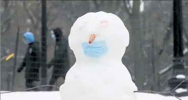  ?? NICOLAUS CZARNECKI PHOTOS / BOSTON HERALD ?? A snowman with a face mask is seen Wednesday on the Public Garden in Boston, while sledders, below, hit the hill on the Common.