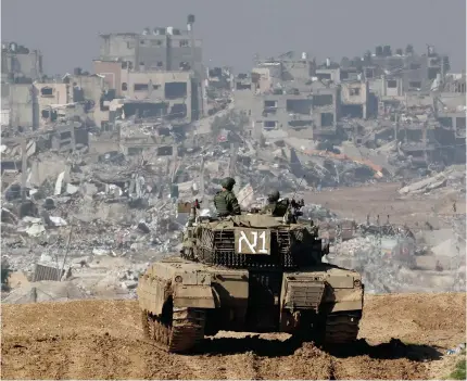  ?? Photo by JACK GUEZ / AFP ?? A picture taken from a position in southern Israel along the border with the Gaza Strip on January 19, 2024 shows an Israeli tank rolling along the fence as damaged buildings are seen in Gaza amid continuing battles between Israel and the militant group Hamas.